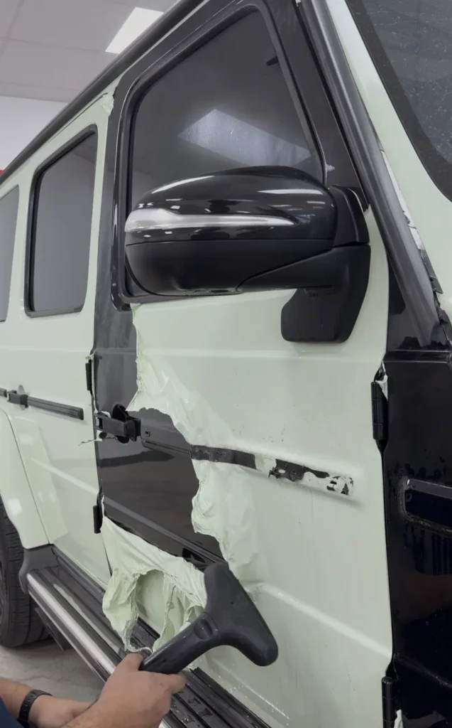 APS technician using steam to remove the green vinyl wrap from a Mercedes G63