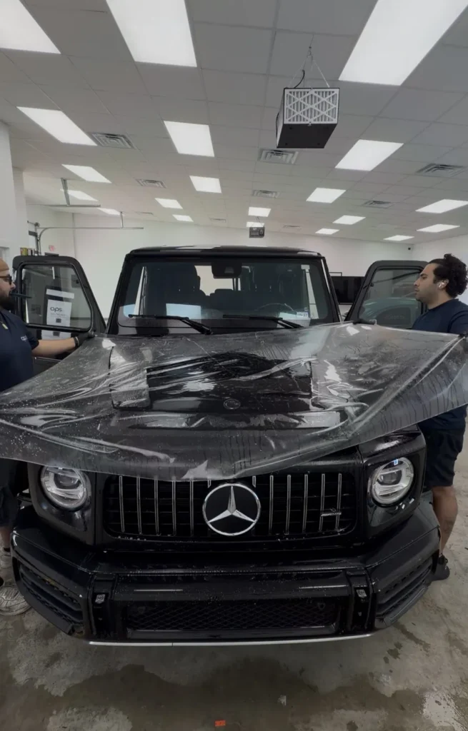 Two APS installers laying XPEL Stealth PPF on a Mercedes G63 hood